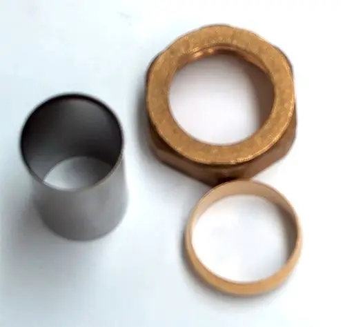 Daikin Zubehör-Set bestehend aus drei metallischen Komponenten: einem zylindrischen Teil, einer sechseckigen Mutter und einem Ring, auf hellem Hintergrund.